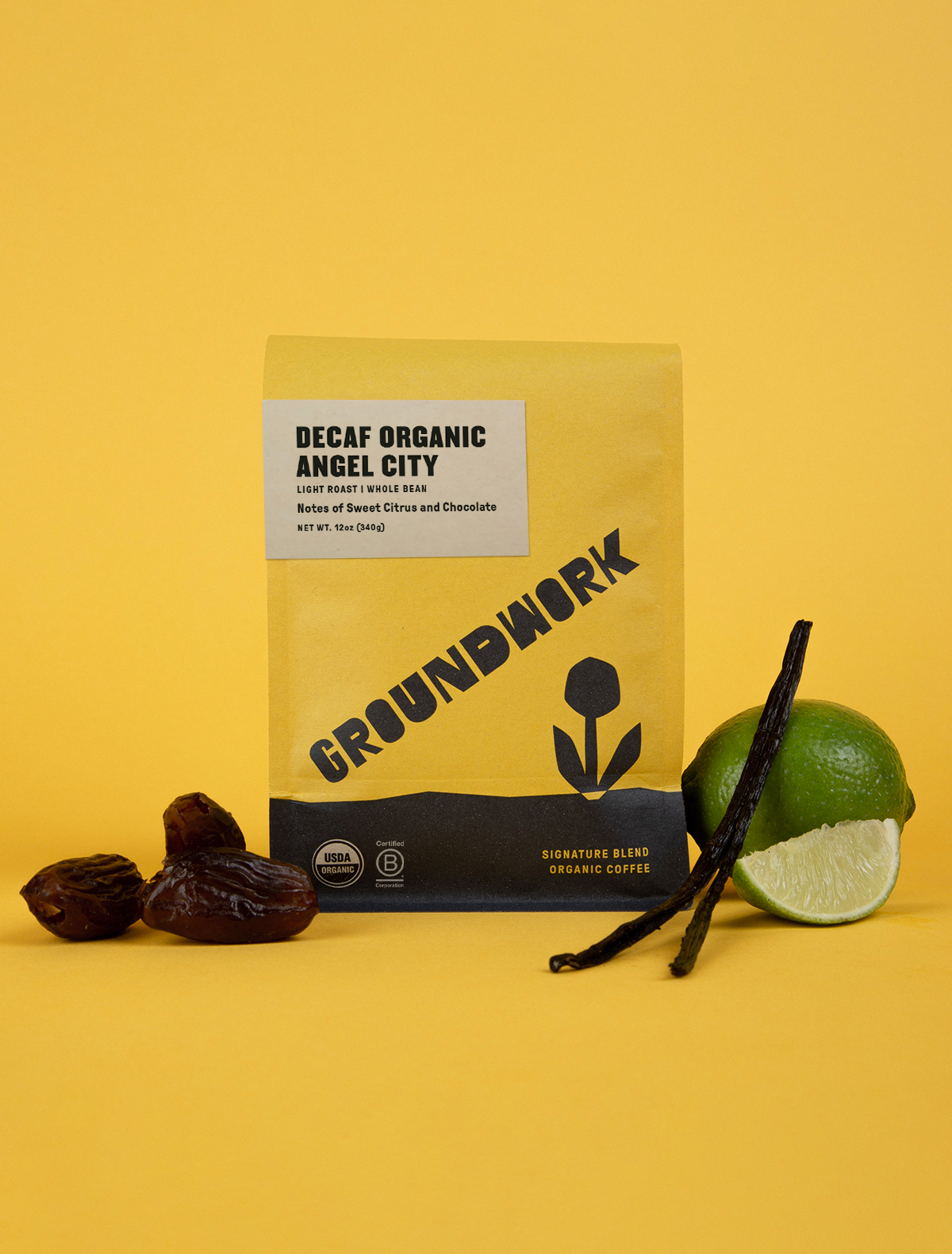 A yellow bag of Groundwork Coffees Decaf Angel City sits on a yellow background, with dates, a lime, and a vanilla bean beside it.