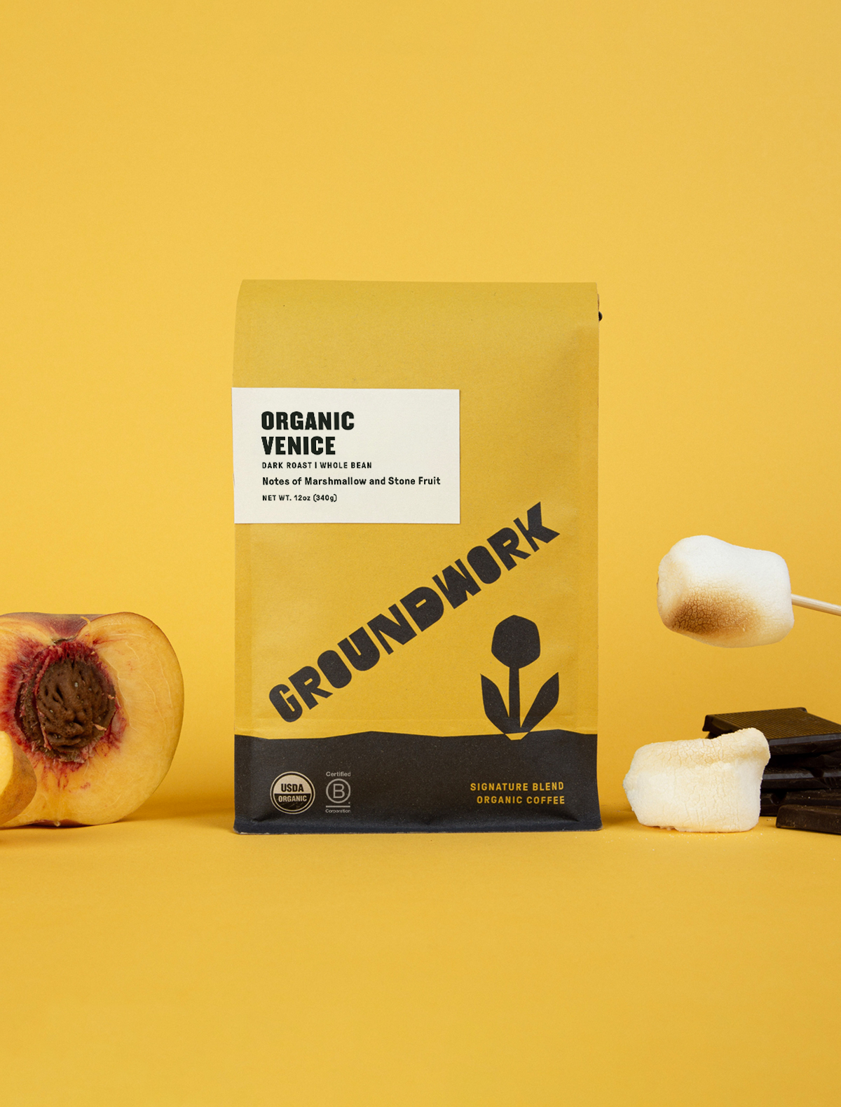 A yellow bag of Groundwork Coffees Venice sits on a yellow surface, beside stone fruit, toasted marshmallows, and chocolate.