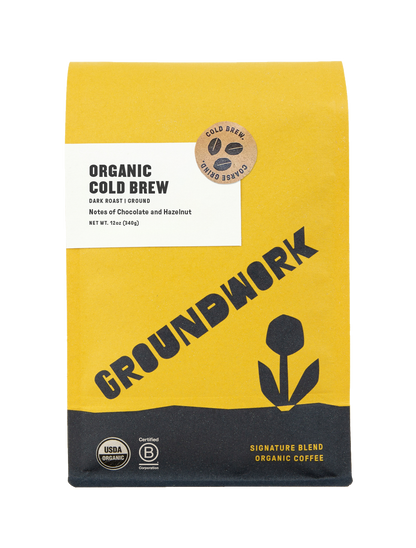 A yellow and black bag of Groundwork Coffee Store Organic Cold Brew Blend, dark roast with chocolate and hazelnut notes, flower graphic, and USDA Organic label.