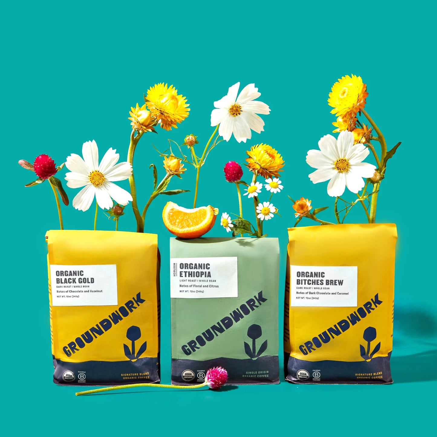 Three vibrant Groundwork Coffee bags—Black Gold, Ethiopia, and Bitches Brew—highlight the Best-Sellers Coffee Bundle against a bright teal backdrop with flowers and an orange slice.