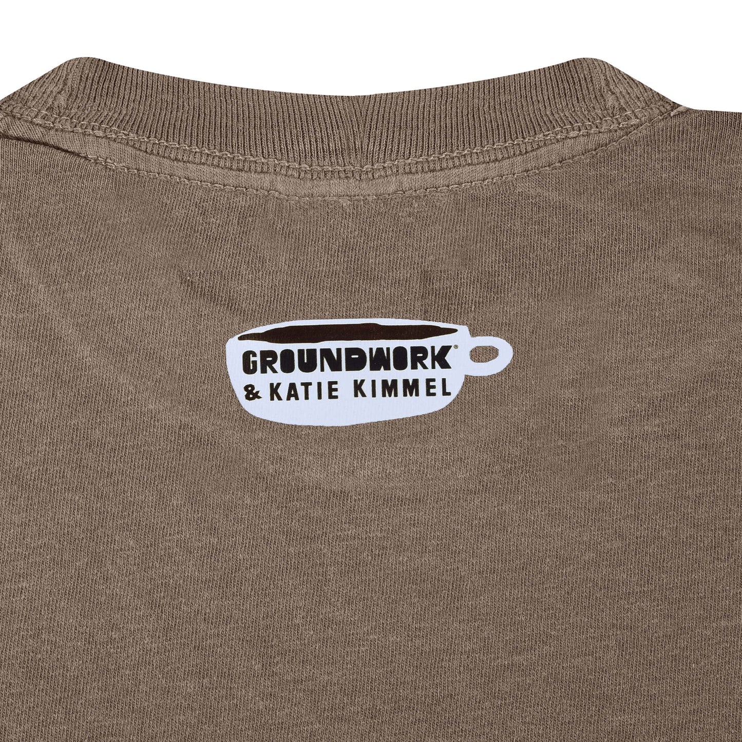 Close up of small white Groundwork & Katie Kimmel coffee cup logo heat pressed on brown fabric