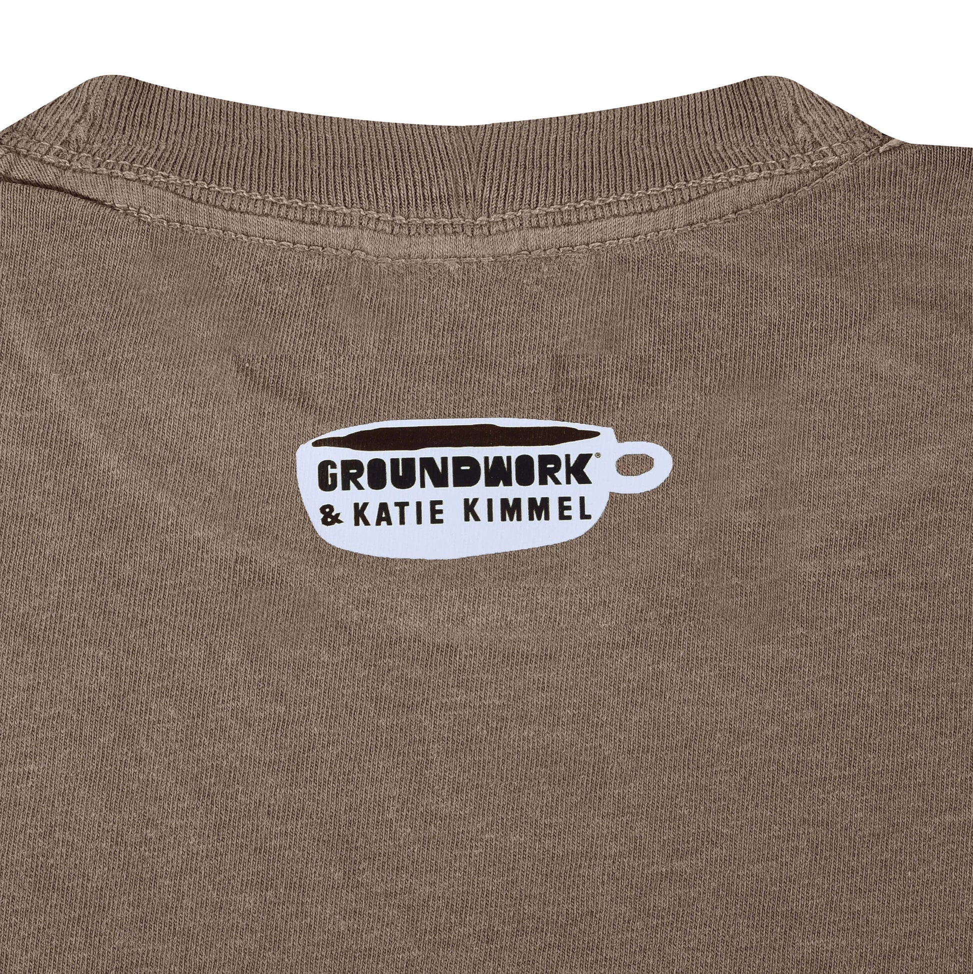 Close up of small white Groundwork & Katie Kimmel coffee cup logo heat pressed on brown fabric