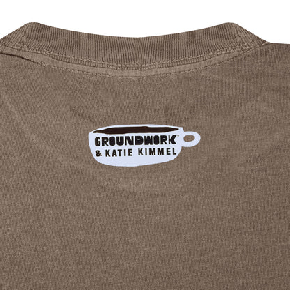 Close up of small white Groundwork & Katie Kimmel coffee cup logo heat pressed on brown fabric