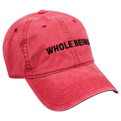 The Whole Being Dad Hat by Groundwork Coffee is a faded red, garment-dyed cotton cap with “WHOLE BEING” embroidered in black on the front.