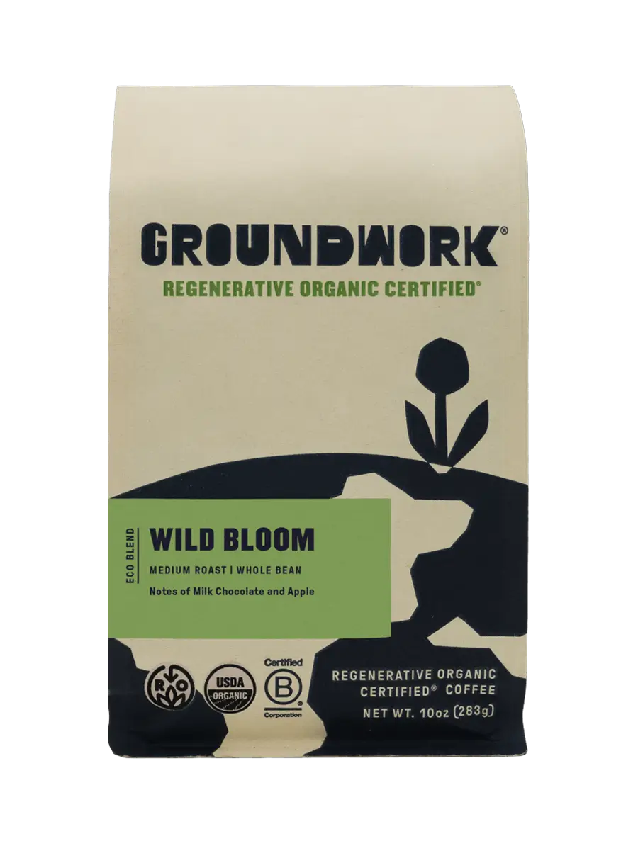 A beige and black bag of Groundwork Coffee Regenerative Organic Certified® Wild Bloom medium roast, with plant art and notes of milk chocolate and apple. Whole bean.