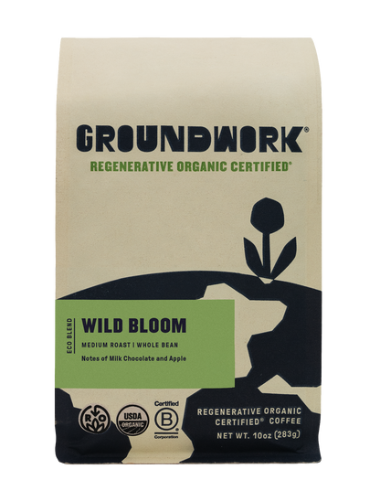 A beige and black bag of Groundwork Coffee Regenerative Organic Certified® Wild Bloom medium roast, with plant art and notes of milk chocolate and apple. Whole bean.