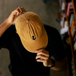 Man wearing Groundwork unstructured 6-panel cotton hat in marigold with embroidered flower logo